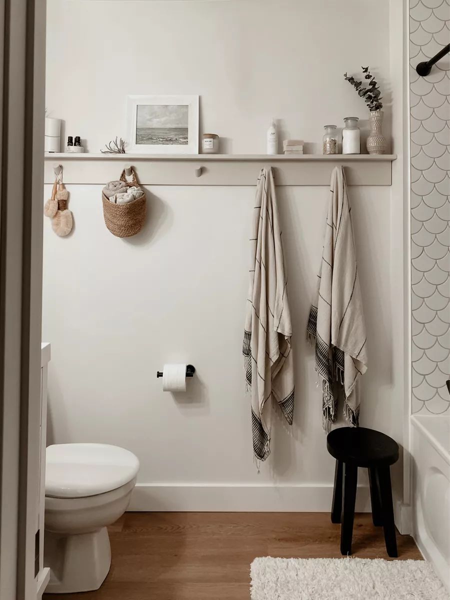 Bathroom shelf and hook rail styled with a woven basket, striped fringed towels, and a small art print — bathroom towel rack basket decor ideas from the By Paige Nicole blog.