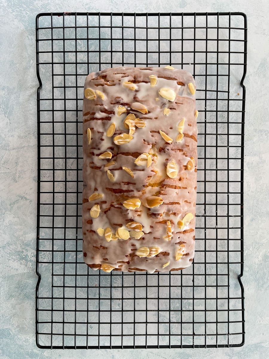 loaf cake topped with icing and almonds on wire rack.