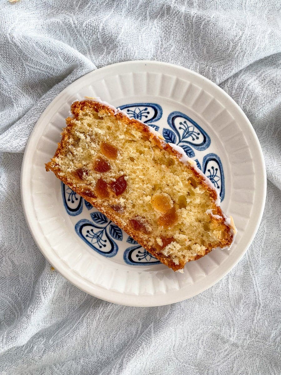 close up of slice of cherry loaf cake on small blue patterned plate.