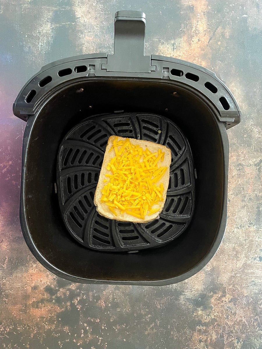bread topped with grated cheese in air fryer basket.