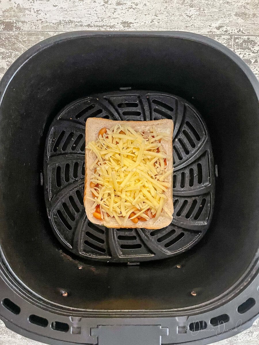 beans and grated cheese on bread in air fryer basket.