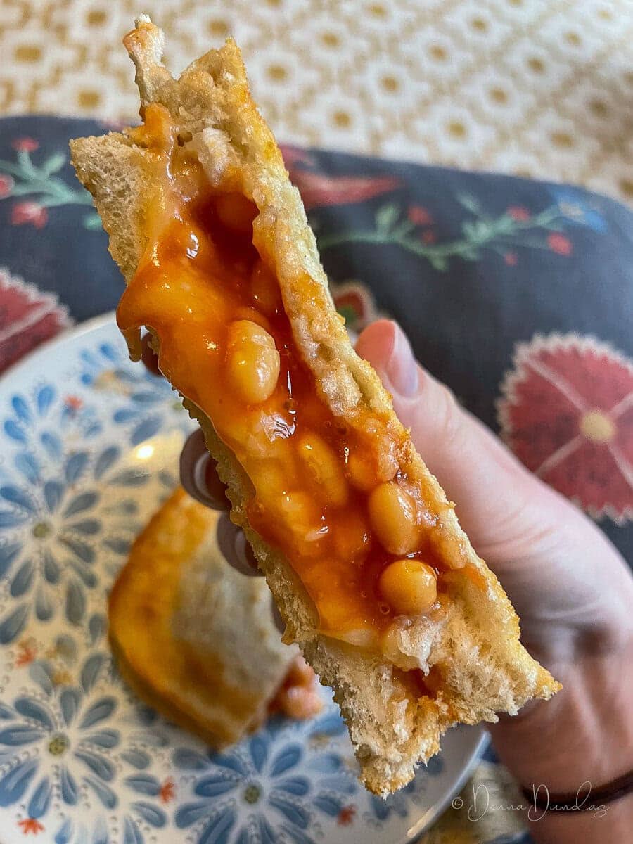 toastie held up to camera, beans pouring out of the middle.