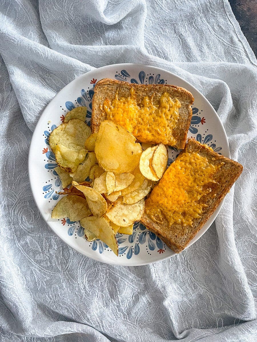 Air fryer cheese and tomato toastie on a plate with crisps.