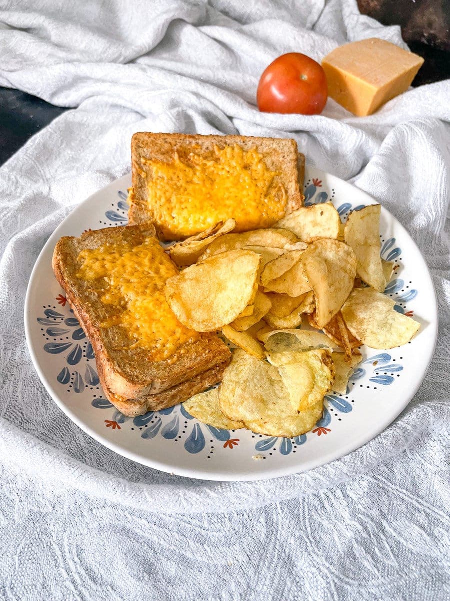 Air fryer cheese and tomato toastie on a plate with crisps.