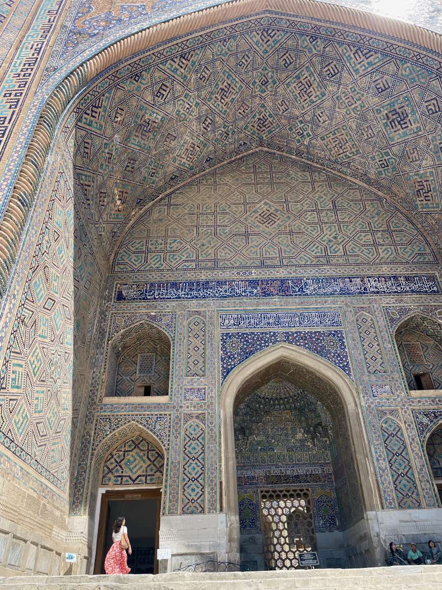 Woman passing through a side door of an imposing madrasah decorated with ancient islamic motifs in samarkand, uzbekistan
