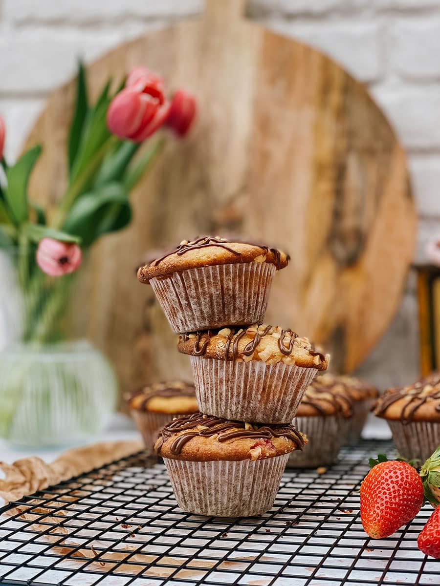 stack of muffins ona. cookie rack, more muffins on the sides, wooden board, scale and flowers on the sides