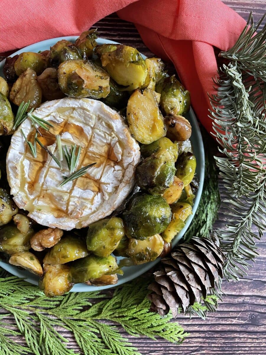 brussel sprouts wreath with camembert in the middle, a napkin, pines and wooden background