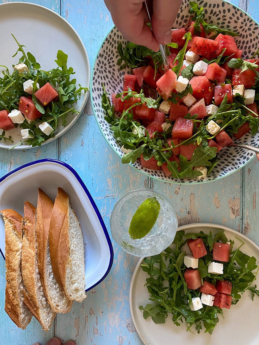 Watermelon and feta salad in three plates, bread on the side on a light blue wooden background