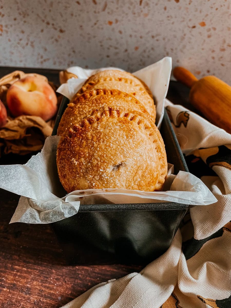 peach hand pies in a tin, peaches on the left and a rolling pin on the right
