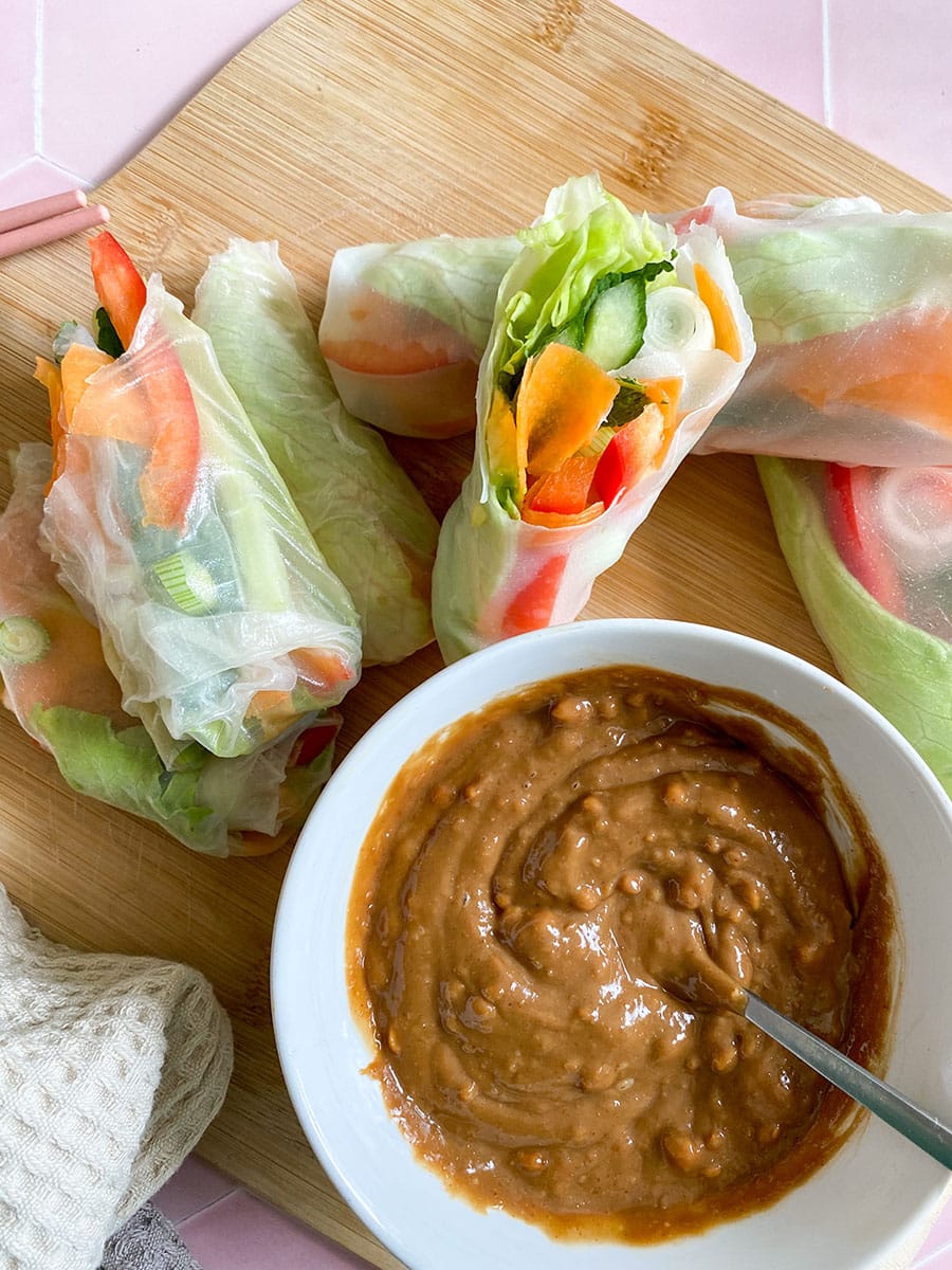 rice paper rolls with vegetables on a wooden board, with peanut dip on the side