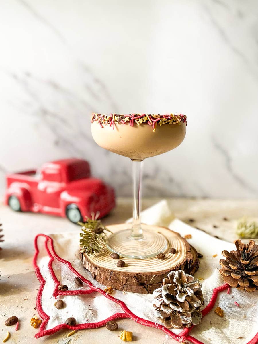 mocha martini cocktail on wooden coasters, a towel under, pinecones, coffee beans and sprinkles around, in the back a red candle, marble background