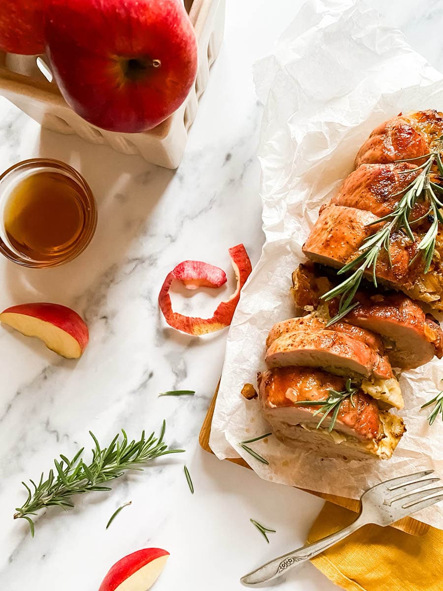 brie stuffed pork tenderloin fillet over parchment paper with apples and a fork over a wooden board