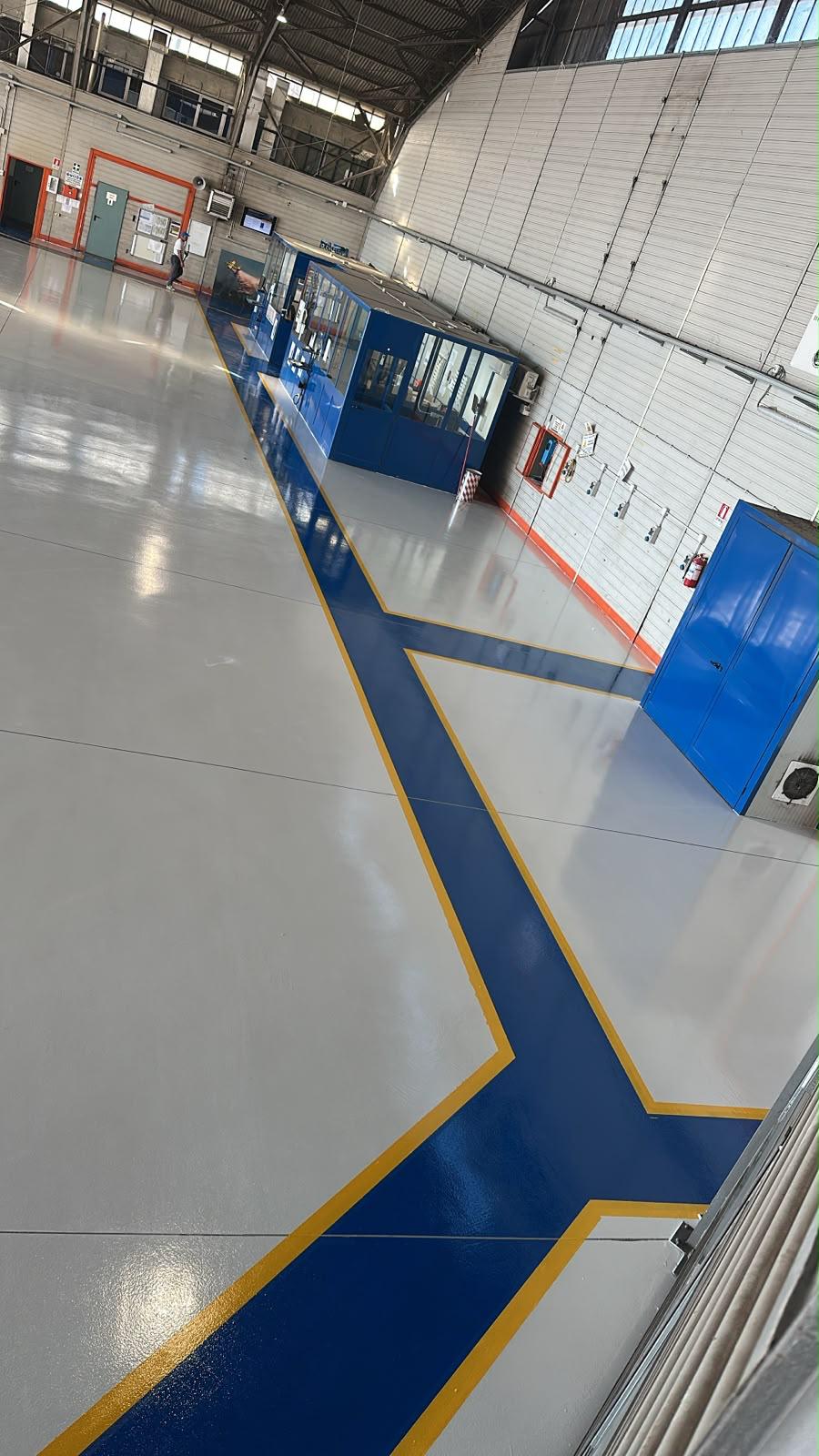 Pavimento in reina grigio chiaro e Percorso in resina con segnaletica direzionale blu e gialla nell'hangar di manutenzione Avincis Aviation