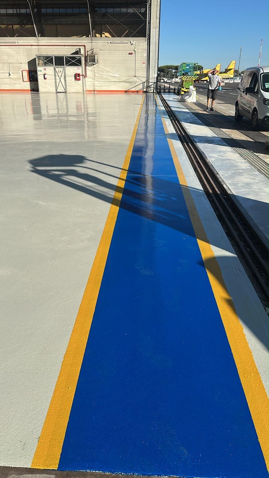 Dettaglio del pavimento in resina blu con bordo giallo all'ingresso dell'area tecnica dell'hangar Avincis di Ciampino