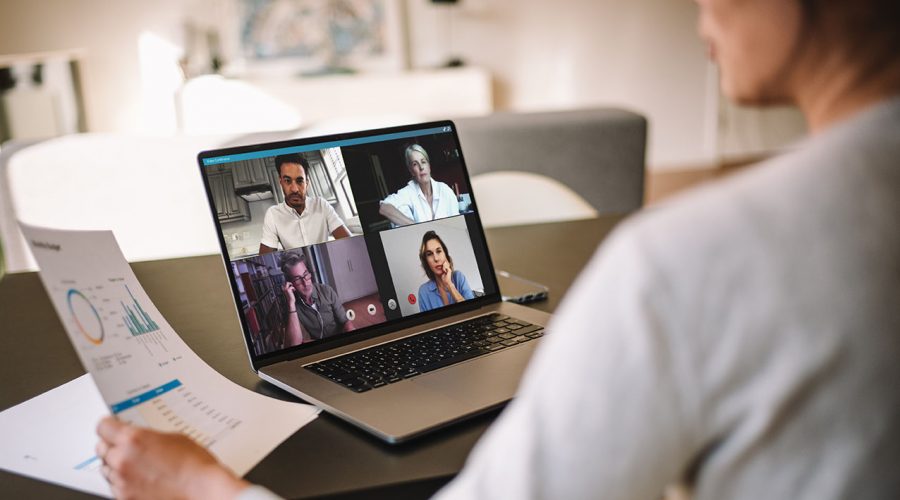 Office colleagues having a video call to discuss few financial reports. Business people working from home having a video conference. Over the shoulder view.