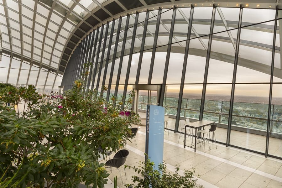 View of a totem sign through the foliage to views of London beyond in the Sky Garden visitor attraction