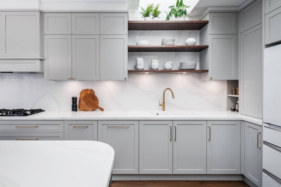 A modern custom-made kitchen with a bespoke design with shaker-style doors and draws. 40mm thick stone bench tops in a light color. and timber-free floating shelves.