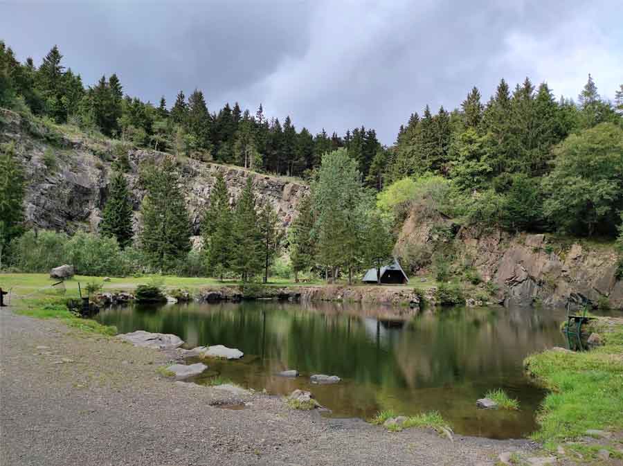 Ansicht Bergsee Ebertswiese. Der See wird von einer Felsenformation umschlossen. Eine kleine Hütte steht am Seeufer. Das Bild ist sehr idyllisch.