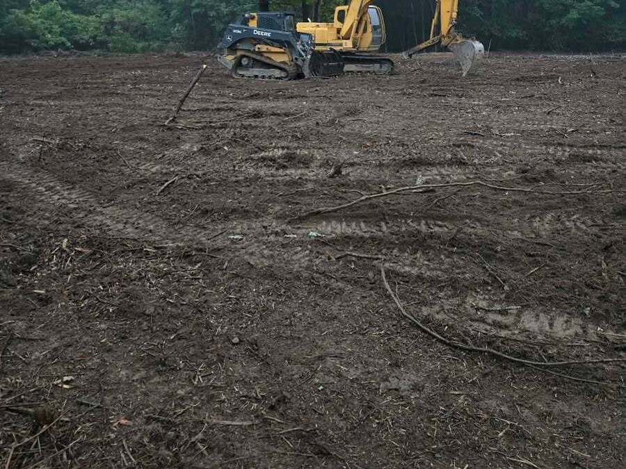 Land Clearing in Jamestown, NY Cleared lot with the stumps out and the ground rough graded, one mature tree left standing at the edge and an excavator working the tree line