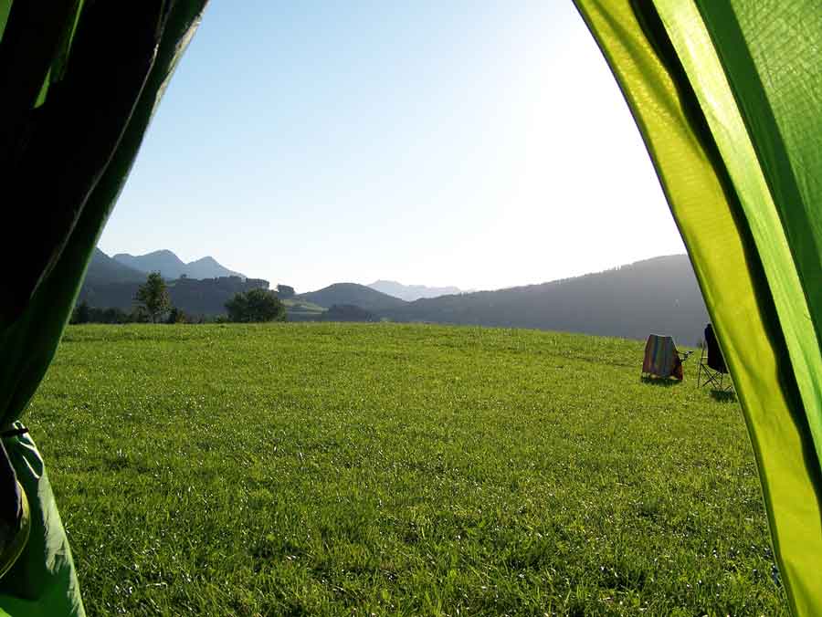 Der Blick aus dem Zelt vermittelt die Freiheit einer Übernachtung auf dem Salzalpensteig. Freier Blick auf die Natur über eine Wiese zu den Bergen, unverstellt und rein.