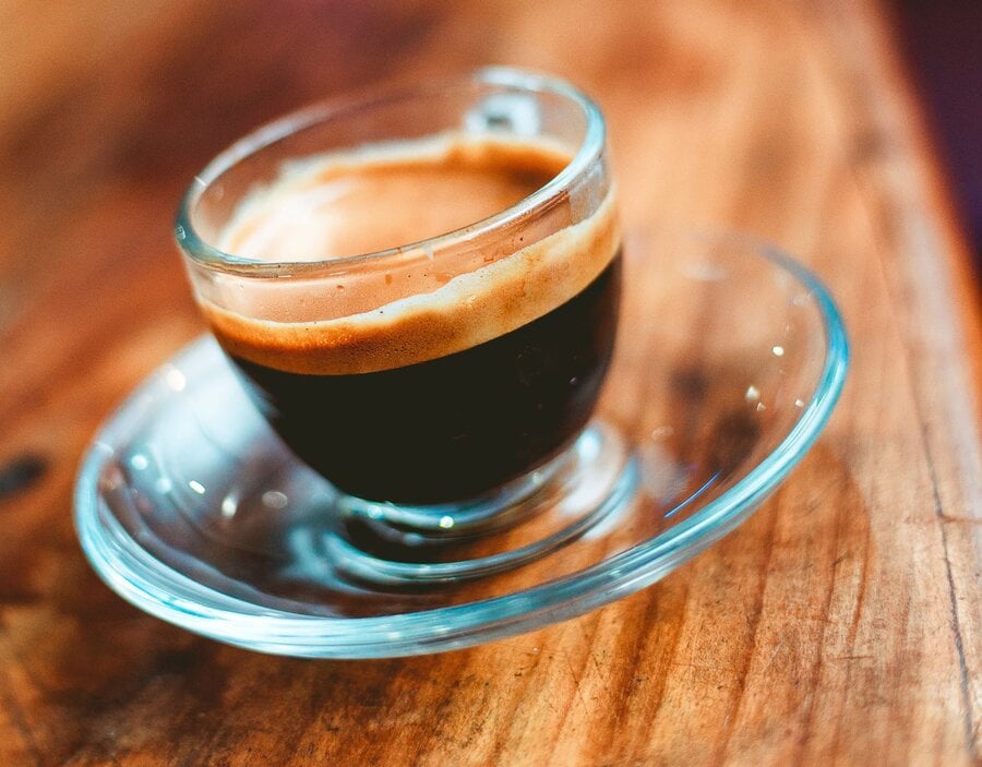 A close-up of a freshly pulled espresso served in a small glass cup on a wooden table.