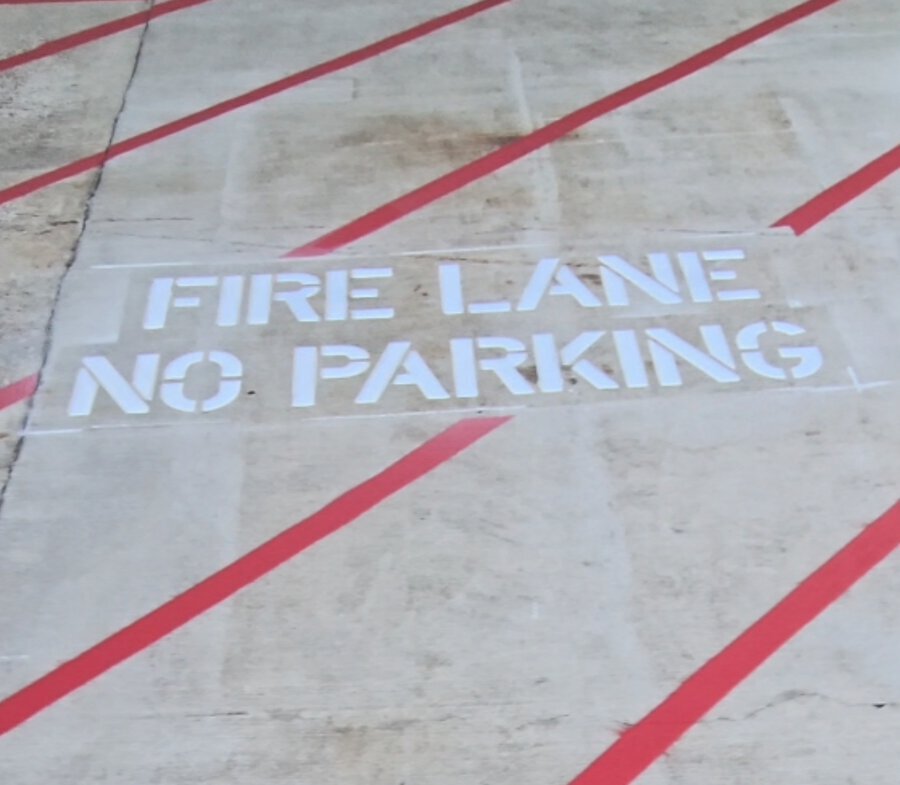 NO PARKING / FIRE LANE stencil painted between red fire lane stripes on concrete