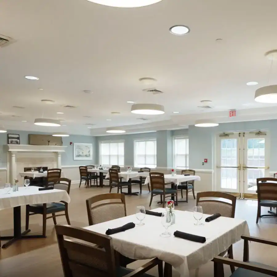 Modern dining area featuring wooden chairs and elegantly set tables with white tablecloths, bright natural light streaming through large windows, and contemporary lighting fixtures.