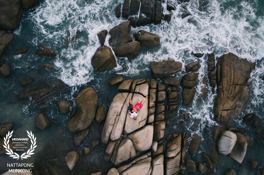Aerial photograph of a couple on coastal rocks surrounded by waves, recognised in Wedaward Collection 46