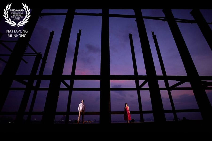 Couple framed by architectural beams against a purple evening sky, recognised in Wedaward Collection 49