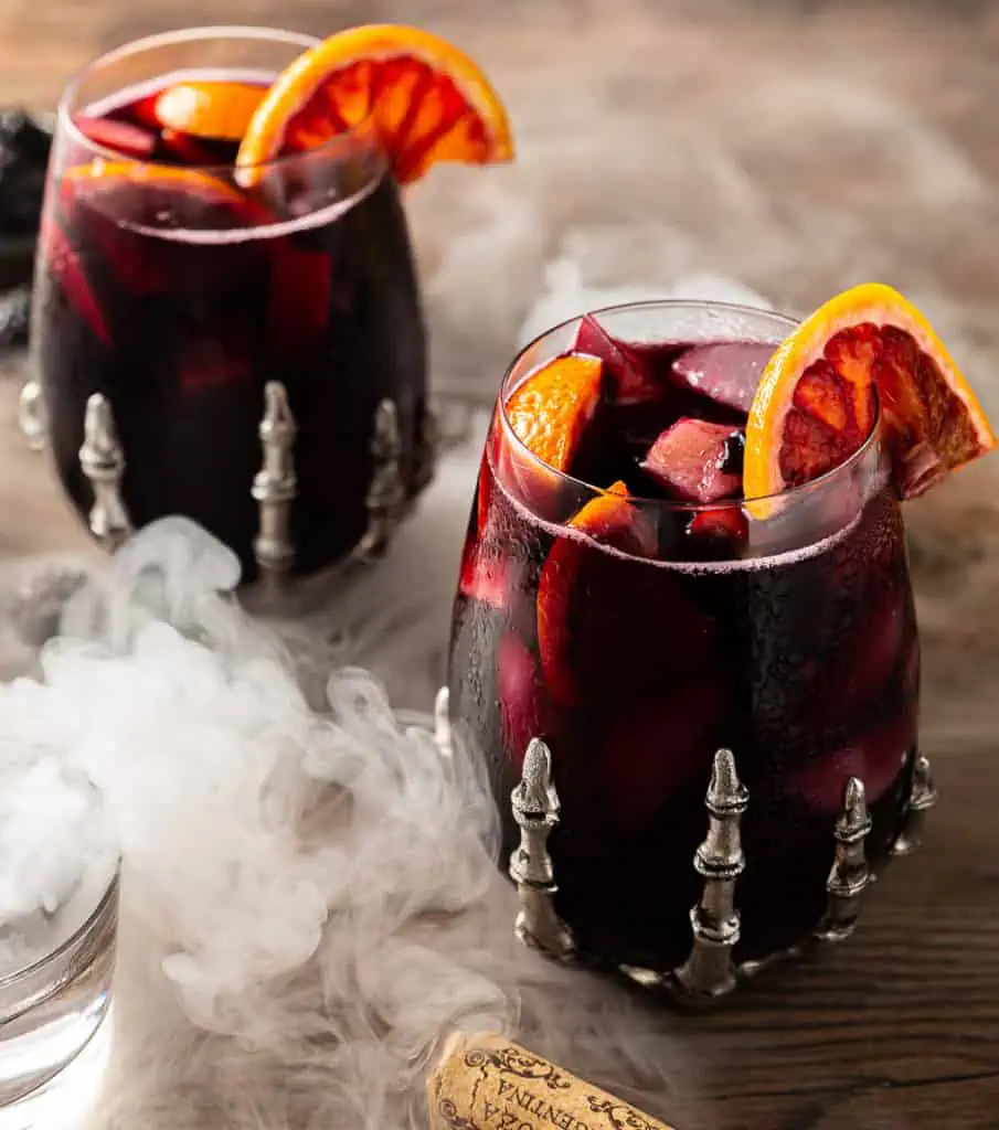 red halloween sangria with apples, oranges, and blackberries with smoke in a skeleton glass