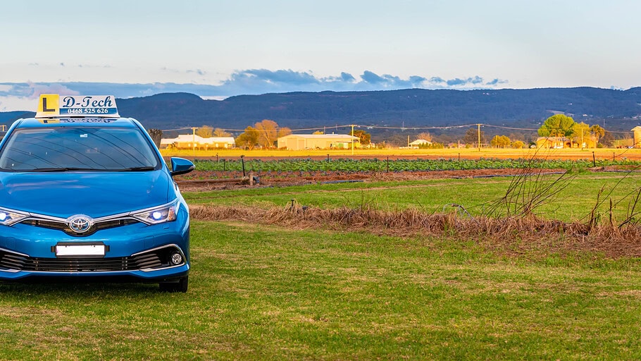 D-Tech driver training car perfectly straight and centered on a scenic country field with spectacular Blue Mountains background view
