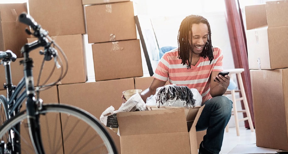 Person sitting among moving boxes and bicycle using a smartphone