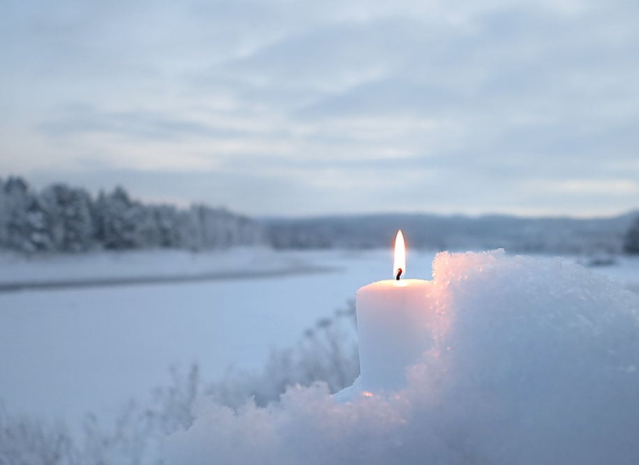 Holiday image with a candle in the white snow next to an ice-covered river. We see Finland from Sweden (Arctic Circle, Napapiiri)