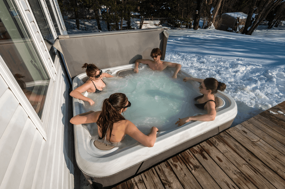 Quatre jeunes personnes se détendent dans un spa installé en extérieur, entouré de neige. 