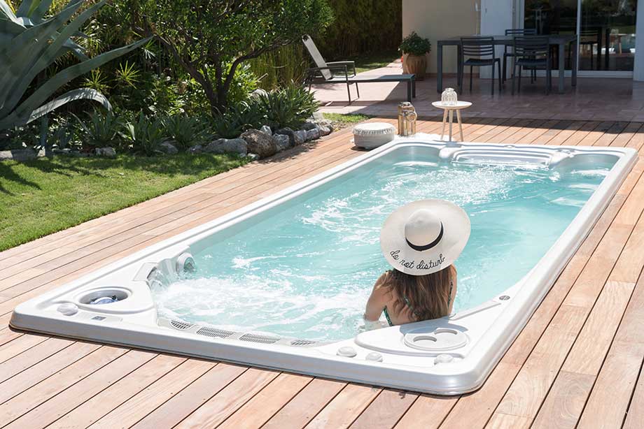 Une femme se détend dans un spa de nage encastré dans une terrasse en bois