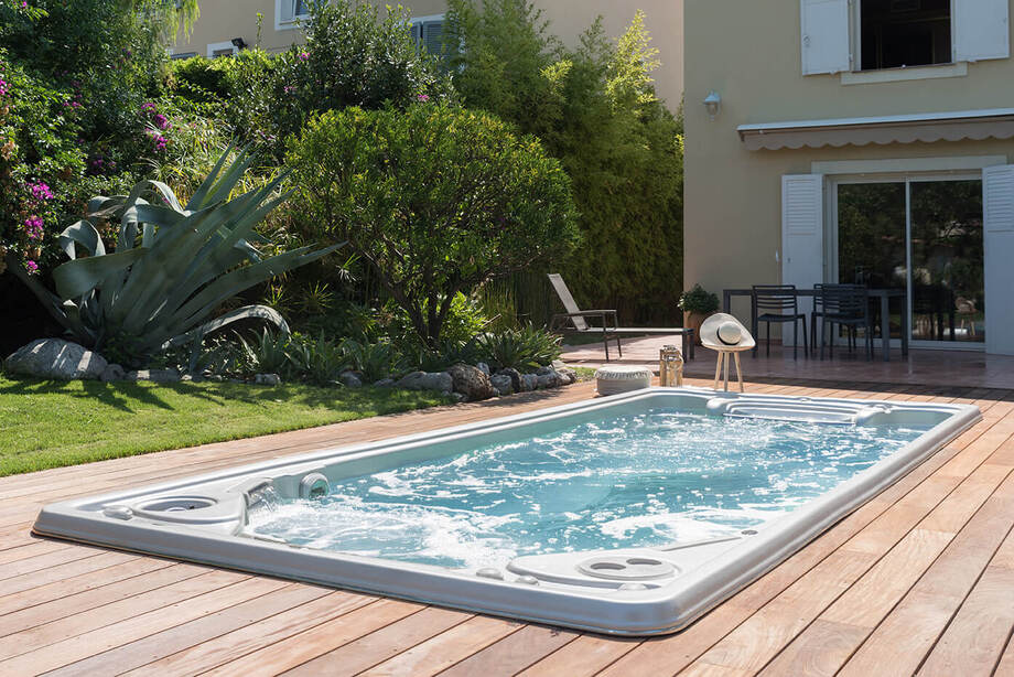 Un spa de nage est encastré dans une terrasse en bois clair, à proximité de la maison. 