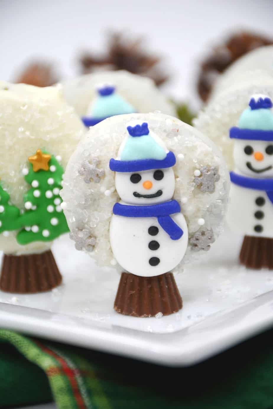 Prepare perfectly decorated Snowman Snow Globe Cookies for the holidays. These sweet, decorative holiday cookies are a must-have for children and adults. This easy cookie recipe is made with OREOS. These chocolate covered OREOS are a fun Christmas Cookie recipe to make and share.