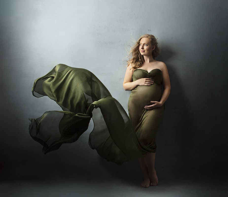 Elegant gravidfotografering av gravid kvinne i grønn kjole som viser magens skjønnhet, med mykt lys og moderne uttrykk for buksefoto av gravide.