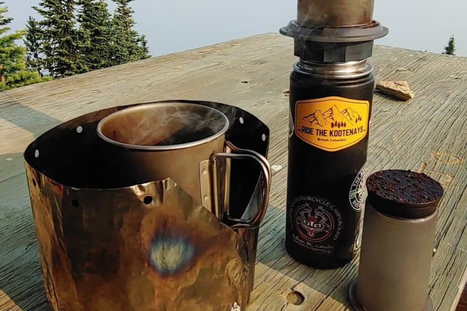 Camping stove and mug and aeropress coffee maker on a table in the mountains