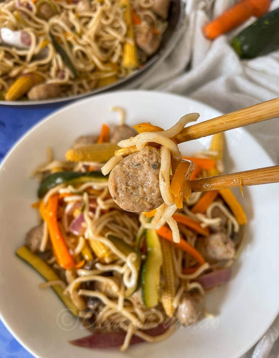 piece of sausage held in chop sticks.
