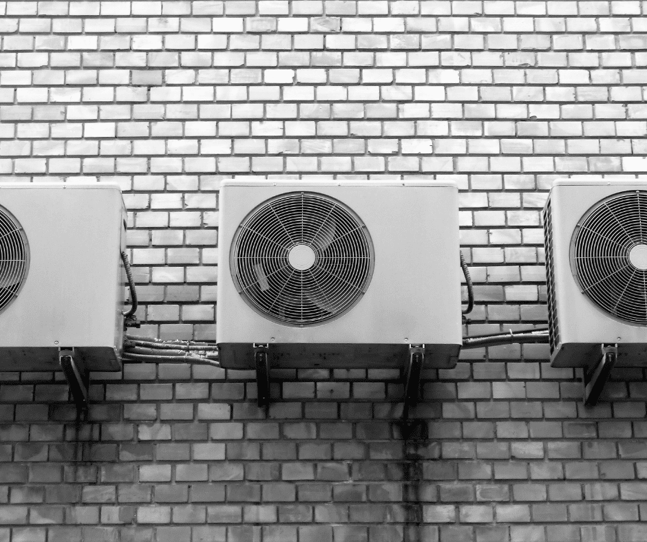 Außeneinheit einer Wärmepumpe mit einer anthrazitfarbenen Schallschutzhaube zur Geräuschreduzierung im Wohngebiet. Stapel von Förderanträgen für die KfW-Förderung und den BAFA-Zuschuss für eine neue Wärmepumpe.