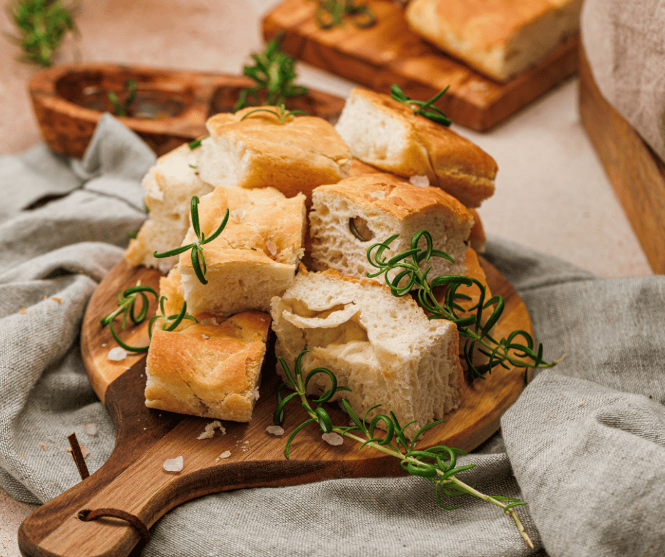Top-down view of cubed rosemary focaccia bread on a wooden board with a small bowl of olive oil dipping sauce.