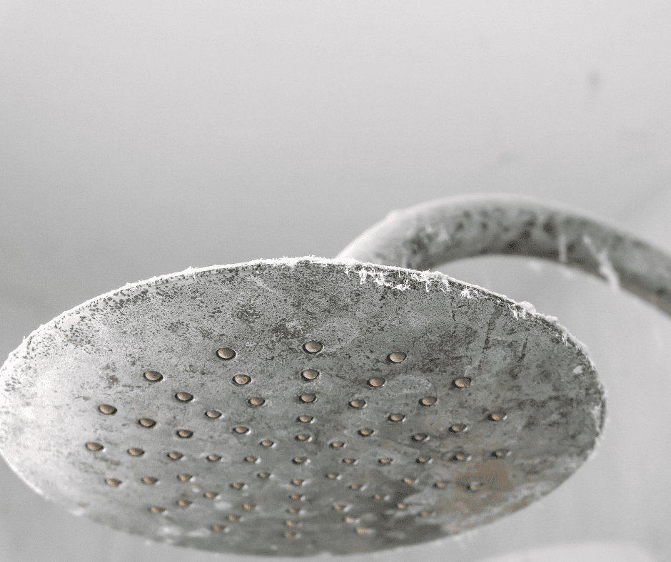 Close-up of a round chrome showerhead covered in white limescale and mineral deposits.