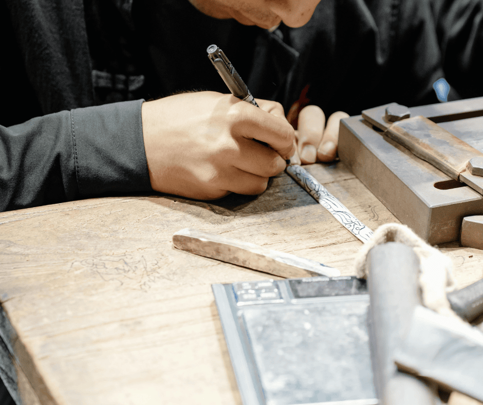 Artist using a fine-liner pen to sketch a custom design on a metal surface before engraving.