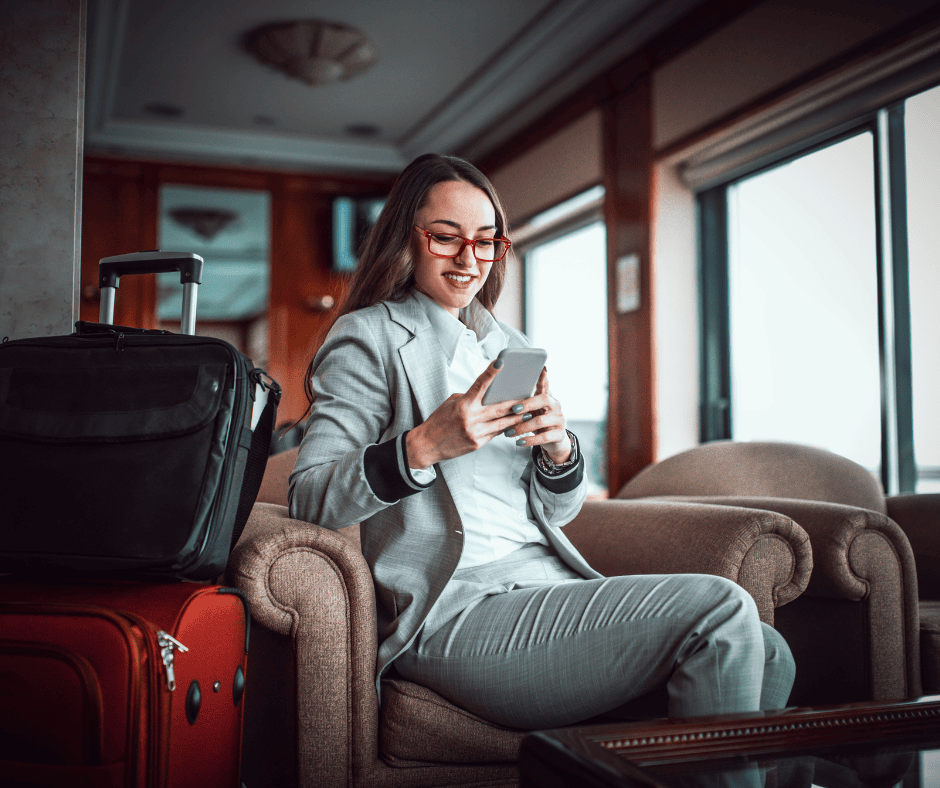 A woman in a grey suit and red glasses sitting in a lounge and looking at her smartphone.