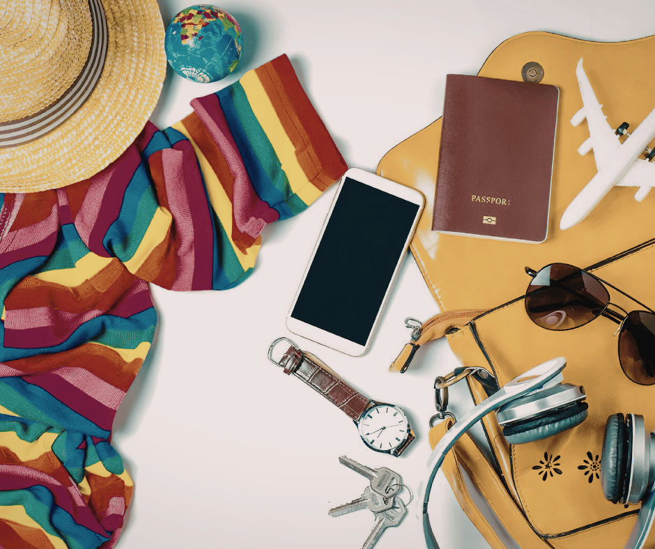 Overhead view of travel essentials including a passport, smartphone, sunglasses, and a sun hat.