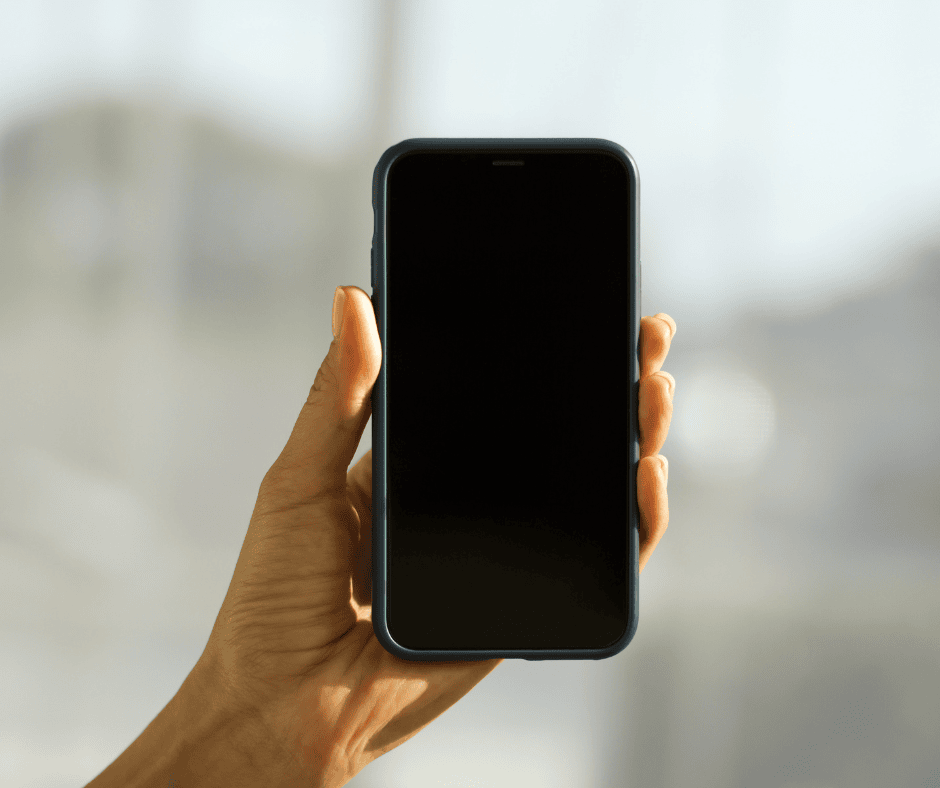 A close-up of a person's hand holding a smartphone with a blank black screen.