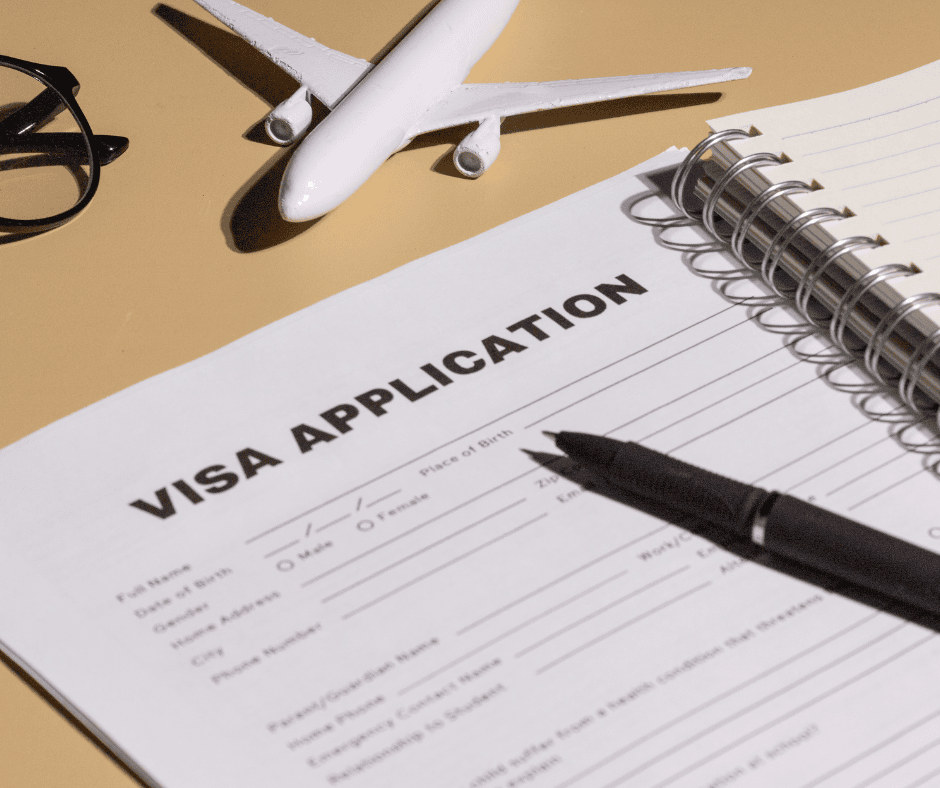 A close-up of a "Visa Application" form on a desk with a black pen, eyeglasses, and a small white model airplane, symbolizing the legal logistics of moving.