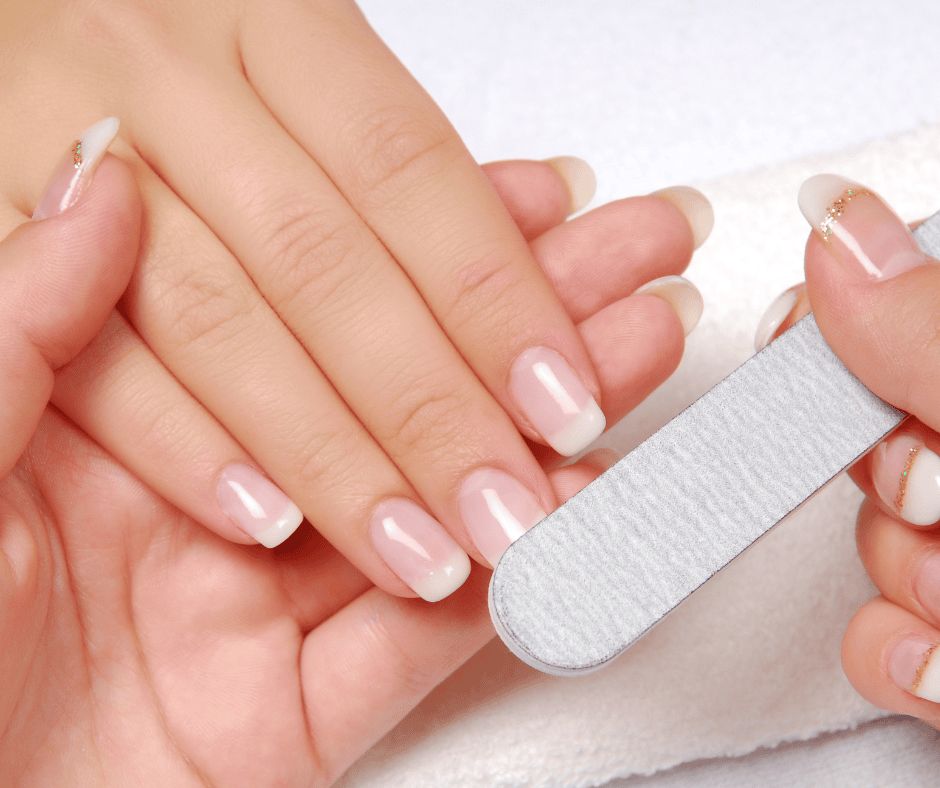 A professional nail technician using a grey zebra-grit file to shape a client's natural French manicure nails.