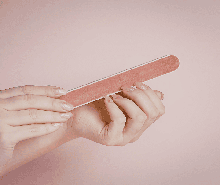 A close-up of hands holding a classic orange-brown emery board against a soft pink background.